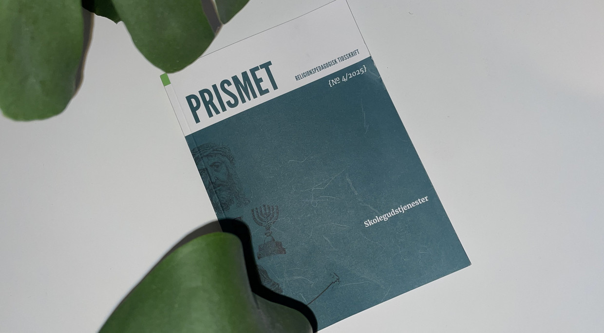 Tidsskriftet Prismet ligger på en hvit overflate under en grønn plante.